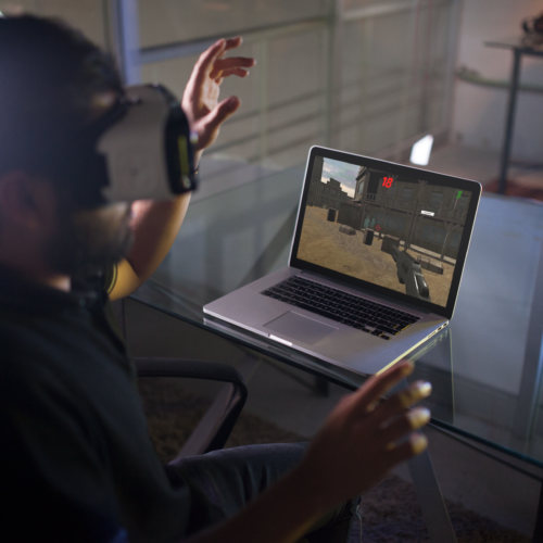 mockup-of-a-young-man-wearing-an-oculus-gear-vr-device-while-his-macbook-pro-is-on-the-desk-a14246